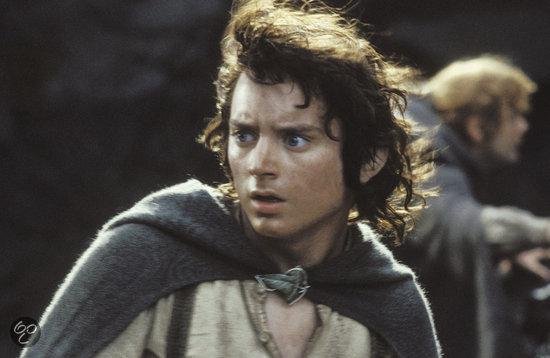 Elijah Wood als Frodo met warrig haar, blauwe ogen en een grijze cape om zijn schouders.