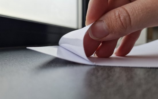 Gros plan d'une main détachant un autocollant, révélant un support blanc.