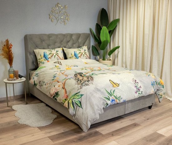 Bed opgemaakt met een lichtgrijs dekbedovertrek met een print van papegaaien, vlinders en bloemen.