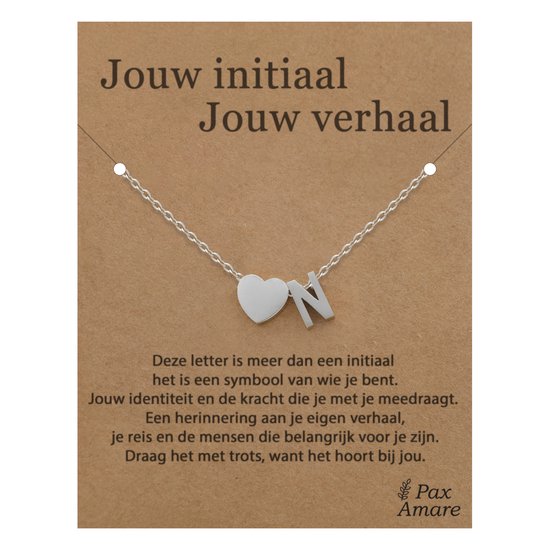 Collier argenté avec un cœur et la lettre N, présenté sur une carte en carton avec du texte.