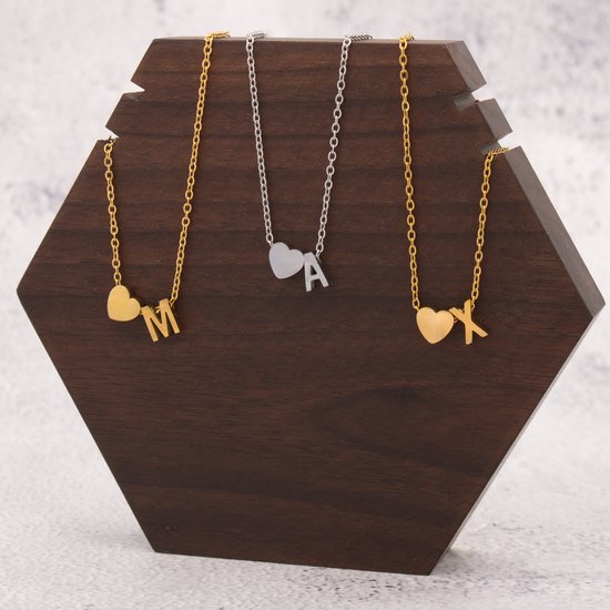 Collier doré avec initiale M et cœur, collier argenté avec initiale A et cœur, collier doré avec initiale K et cœur.