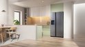 Zilverkleurige Amerikaanse Samsung koelkast met waterdispenser in een lichte, moderne keuken met houten meubels.