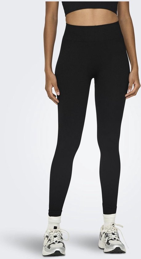 Model met zwarte, nauwsluitende sportlegging met hoge taille en geribd patroon, en witte sneakers.