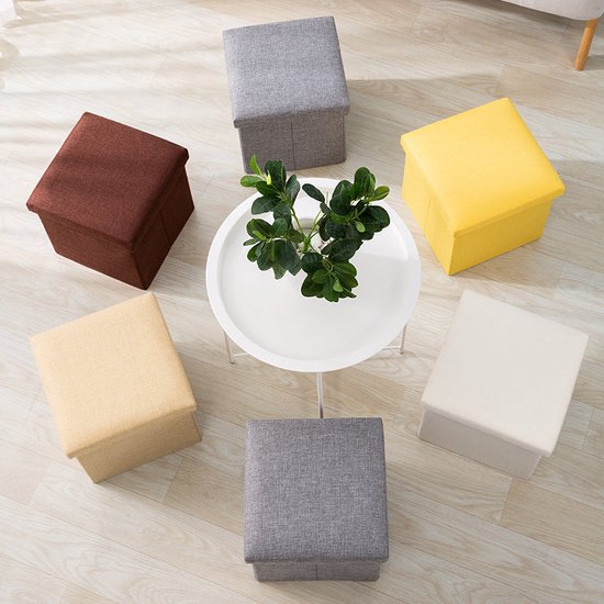 Zes opbergpoefjes in verschillende kleuren (grijs, bruin, geel, crème) rond een witte salontafel.
