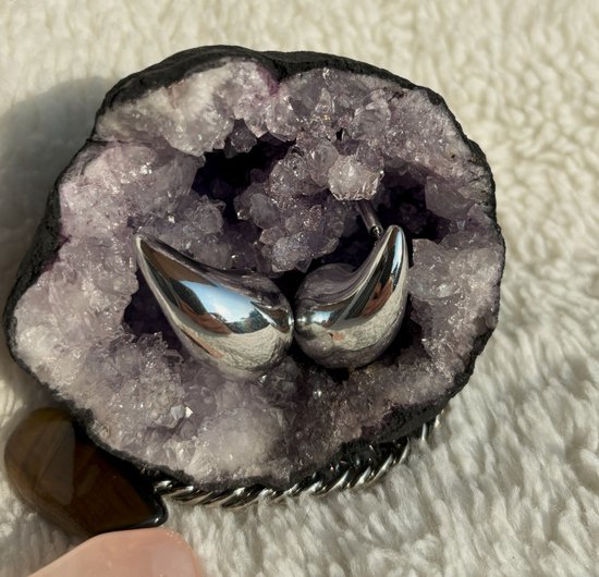 Twee zilverkleurige, waterdruppelvormige oorbellen in een amethistgeode.