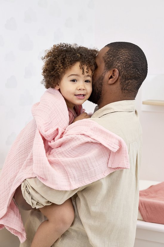 Lachend kindje in een zachtroze swaddle op de schouder van een man.