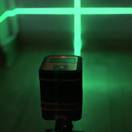 Een zwarte en oranje kruislijnlaser met groene laserlijnen op een muur en vloer.