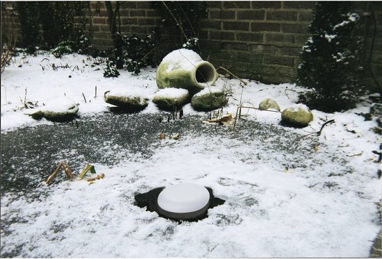 Witte ijsvrijhouder op de bodem van een bevroren vijver, bedekt met sneeuw. Vage achtergrond met stenen en een vaas.