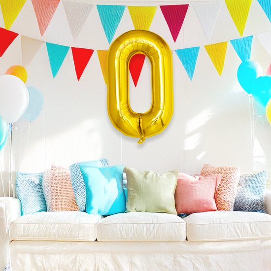 Gouden ballon met cijfer 0 hangt aan een muur met slingers en een bank.