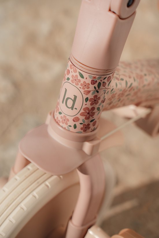Detail van de bloemenprint met 'ld.' logo op de stuurkolom van de roze driewieler.