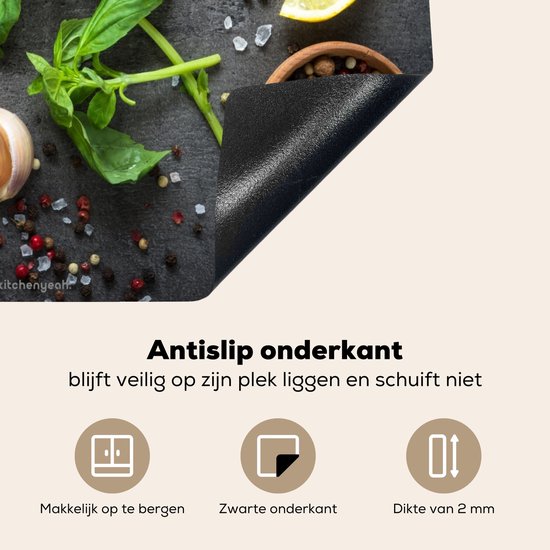 Zwarte inductiebeschermer met betonprint, detail van de antislip onderkant, met kruiden, knoflook, citroen en peperkorrels.