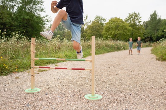 Jongen springt over houten hindernisbaan met rode en groene balken, op een bospad.