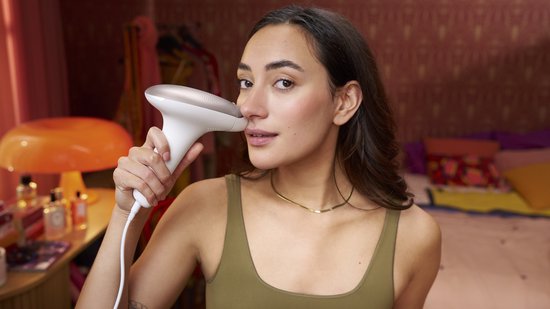 Vrouw met donker haar gebruikt het witte Philips Lumea IPL ontharingsapparaat op haar gezicht.