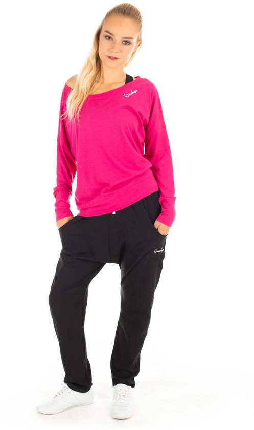 Model in een roze longsleeve met wijde boothals en een zwarte broek met logo.