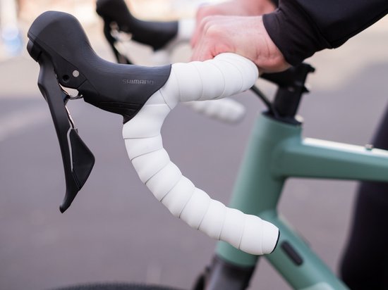 Fietsstuurende met Shimano versnellingen en wit stuurlint, gedragen door handen.