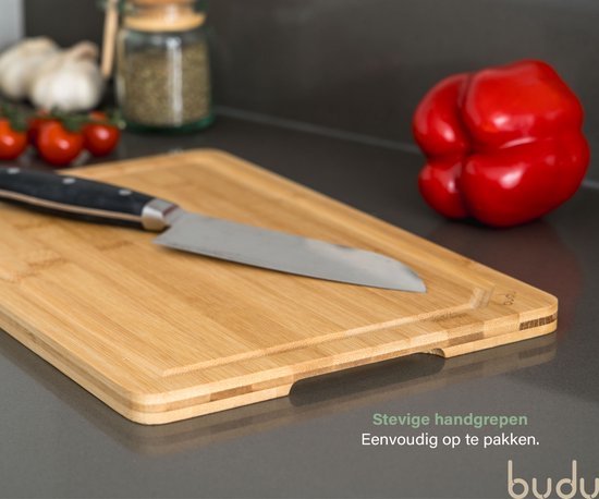 Een Budu bamboe snijplank met een mes en gesneden tomaten. De plank heeft een sapgeul en handgrepen aan de zijkant.