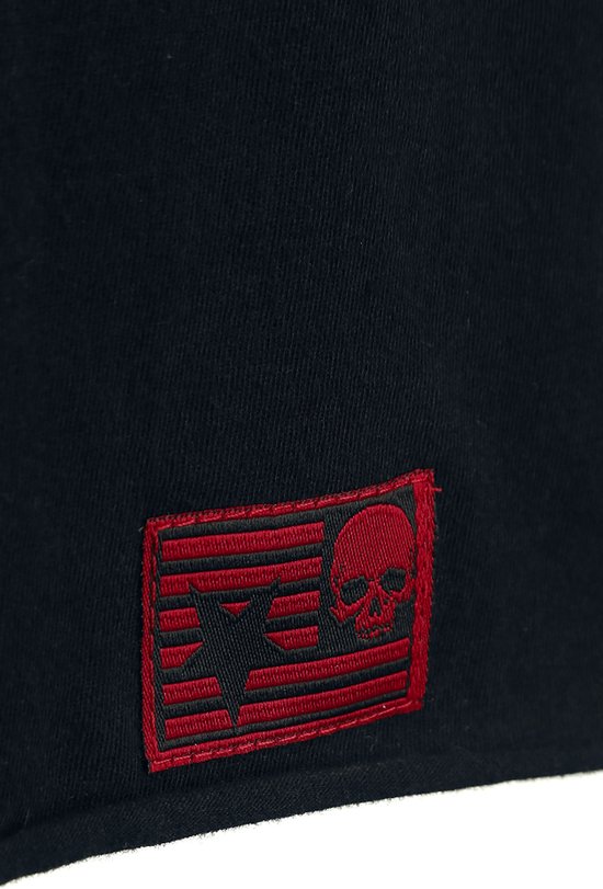 Detail van een zwart jurkje met een rood geborduurd label met een doodshoofd en ster op een gestreepte achtergrond.