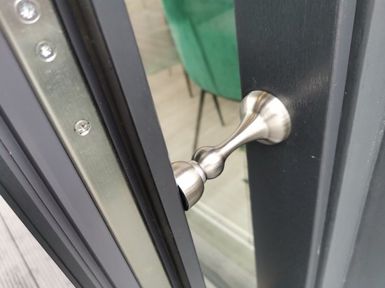 Zilverkleurige, geborstelde metalen deurstopper met bolvormige magnetische kop, gemonteerd op een donkergrijze deurpost.