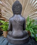 Achterkant van een zwart Boeddhabeeld in meditatiehouding, zittend op een sokkel.