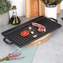 Zwarte gietijzeren grillplaat met ribbels, met een stuk vlees, knoflook en tomaat.