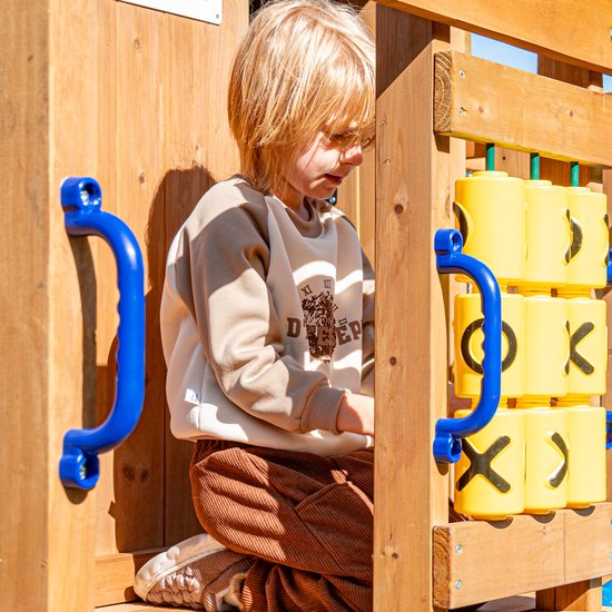 Jongen met bril in beige trui en bruine corduroy broek speelt met geel tic-tac-toe spel op houten speeltoestel.