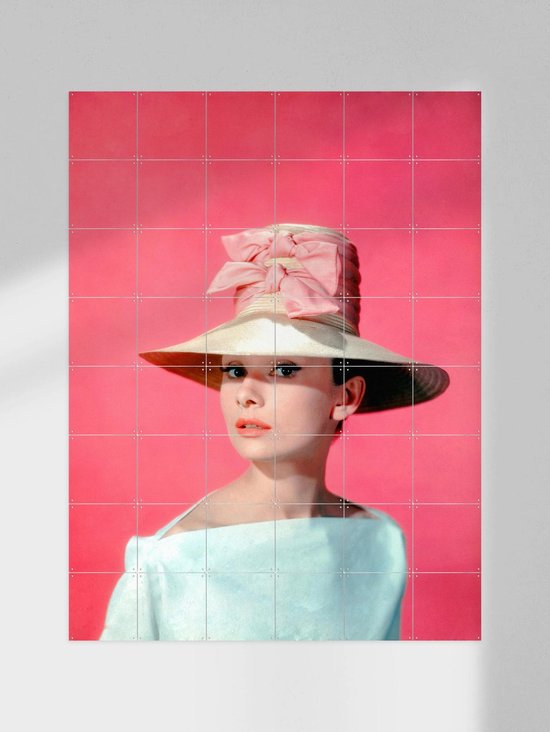 Audrey Hepburn portant un grand chapeau de paille avec un nœud rose, une robe bleu pâle épaules dénudées, sur fond rose.