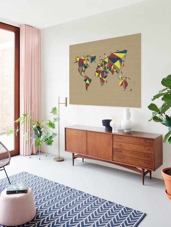 Carte du monde abstraite aux polygones colorés, suspendue au-dessus d'un buffet en bois dans un salon avec des plantes.