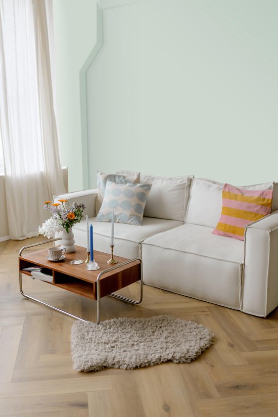 Woonkamer met een witte bank, saliegroene muur en houten vloer.