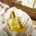 Glazen fles Nuxe Huile Prodigieuse liggend op een witte blouse.