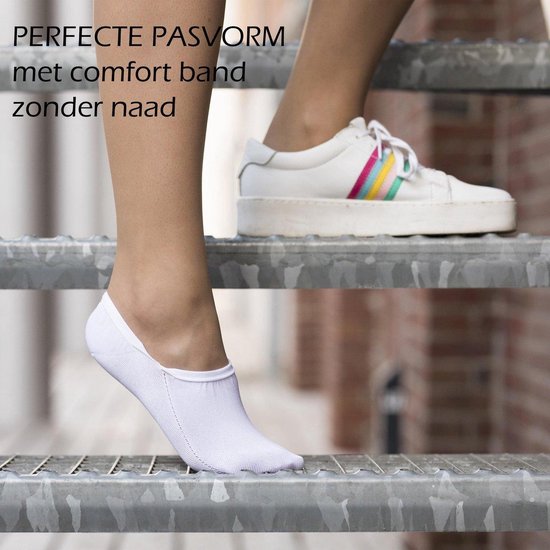 Een vrouw draagt witte onzichtbare sokken en witte sneakers met regenboogstrepen terwijl ze op een metalen trap loopt. 'PERFECTE PASVORM met comfort band zonder naad'.