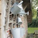 Zinken gieters en emmers hangend aan een houten rek voor een bakstenen muur.