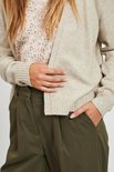 Close-up van een beige gebreid vest, gedragen over een bloemenprint top.