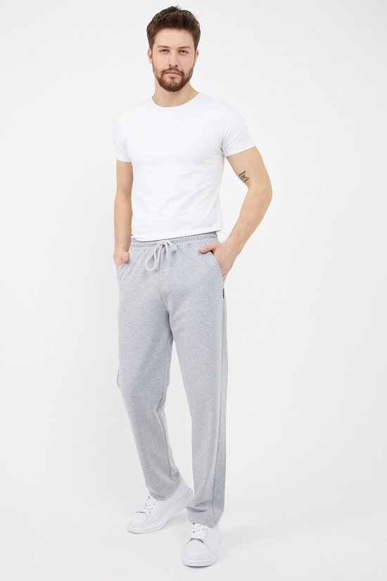 Man met grijze joggingbroek, witte t-shirt, witte sneakers. Broek met koord en zakken.