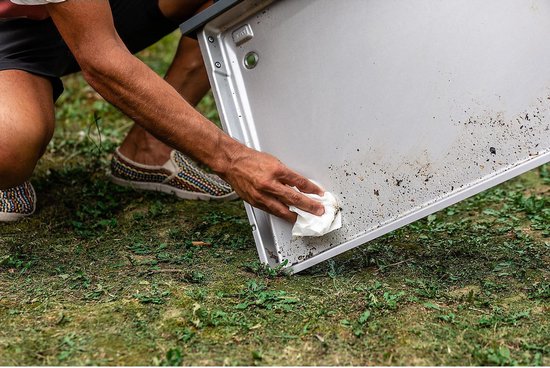 Een hand veegt met een doekje vuil weg van de binnenkant van een barbecueklep.