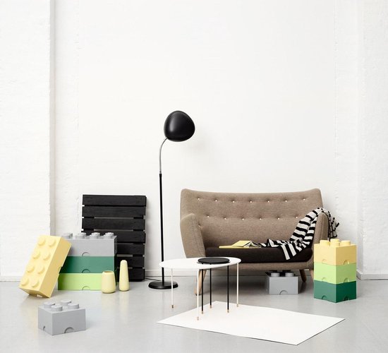 Woonkamer met grijze bank, zwarte vloerlamp en LEGO opbergdozen in geel, groen en grijs.