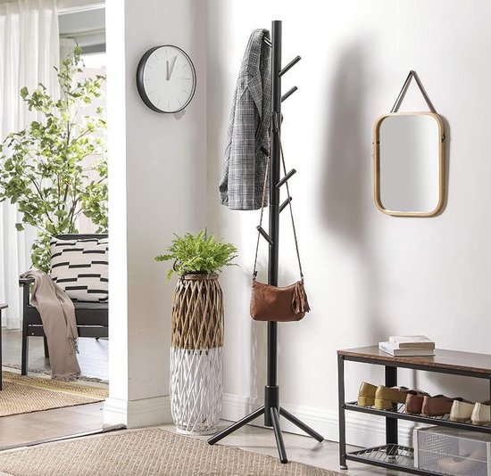Zwarte staande kapstok met een jas en tas aan hangen, in een hal met plantenbak, spiegel en schoenenrek.