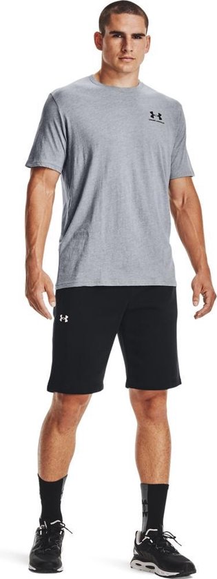 Man met grijze Under Armour t-shirt en zwarte korte broek. Grijs t-shirt met zwart Under Armour logo links op de borst.