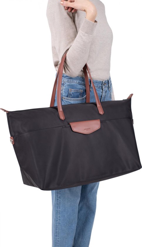 Une femme porte un grand sac de voyage noir avec anses marron et rabat en cuir.