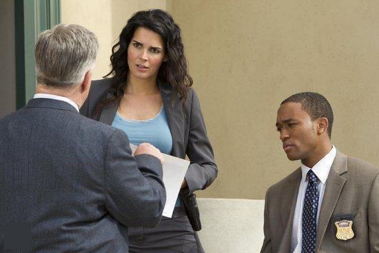 Detective Jane Rizzoli in grijs pak met blauwe top spreekt met een collega. Rechercheur kijkt toe.
