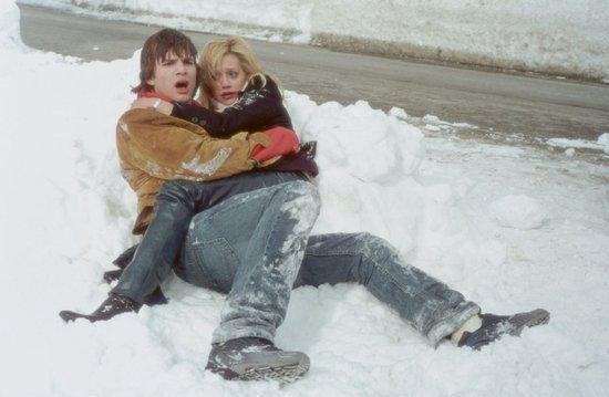 Een man draagt een vrouw in de sneeuw. Ze zien er verbaasd uit.