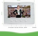 7 inch kleurenscherm van een video-intercom met een vrouw in een zwart pak voor een bruin huis. Knoppen voor livebeeld, deuropen, poort open, spreken en microfoon.