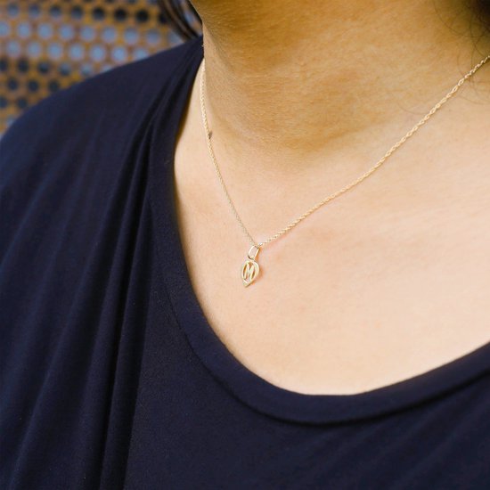 Vrouw draagt een gouden hartvormige hanger met de letter M aan een dunne ketting bij een donkerblauw shirt.