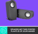 Twee grijze Logitech speakers op een paarse achtergrond. "Speakers met twee posities, plaats ze op jouw manier."