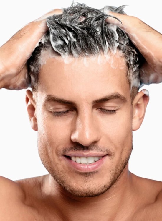 Man met gesloten ogen die zijn haar wast met schuimende shampoo.