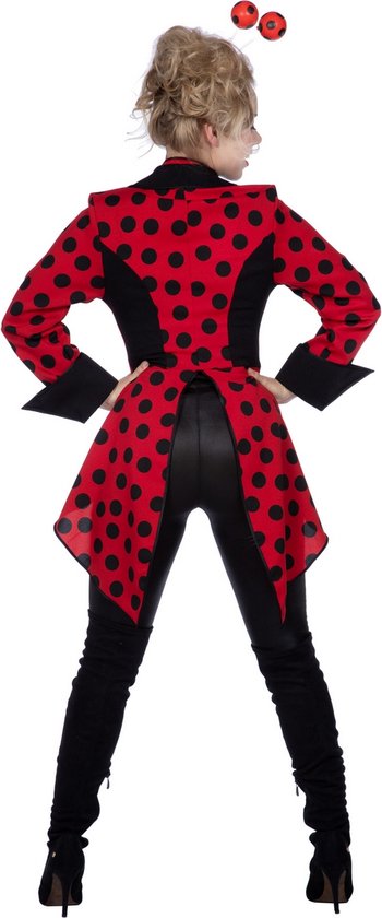 Zijaanzicht van vrouw in rode met zwarte stippen jas, zwarte blouse, leren broek en laarzen. Rode antenne met bolletjes op haarhoofd.