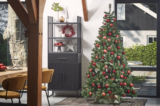 Een sfeervol ingerichte woonkamer met een grote, versierde kunstkerstboom met rode ballen, een kast en een eettafel.