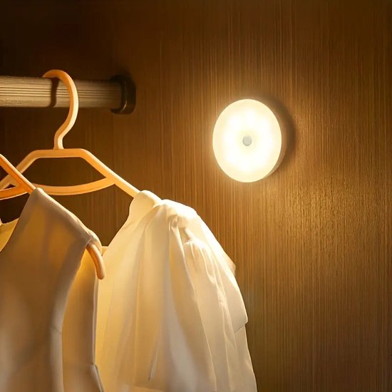 Ronde, witte, oplaadbare kastlamp met zachte gloed, gemonteerd op een houten kastwand.