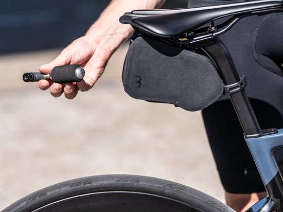 Handen gebruiken een zilveren CO2-patroon met zwarte hoes voor een fietsband onder het zadel.