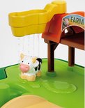 Close-up van de John Deere boerderij speeltafel: water stroomt uit een gele bak op een speelgoedkoe.