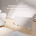 Witte glazen convectorverwarming met digitaal display in een sfeervol ingerichte woonkamer met bank en salontafel.